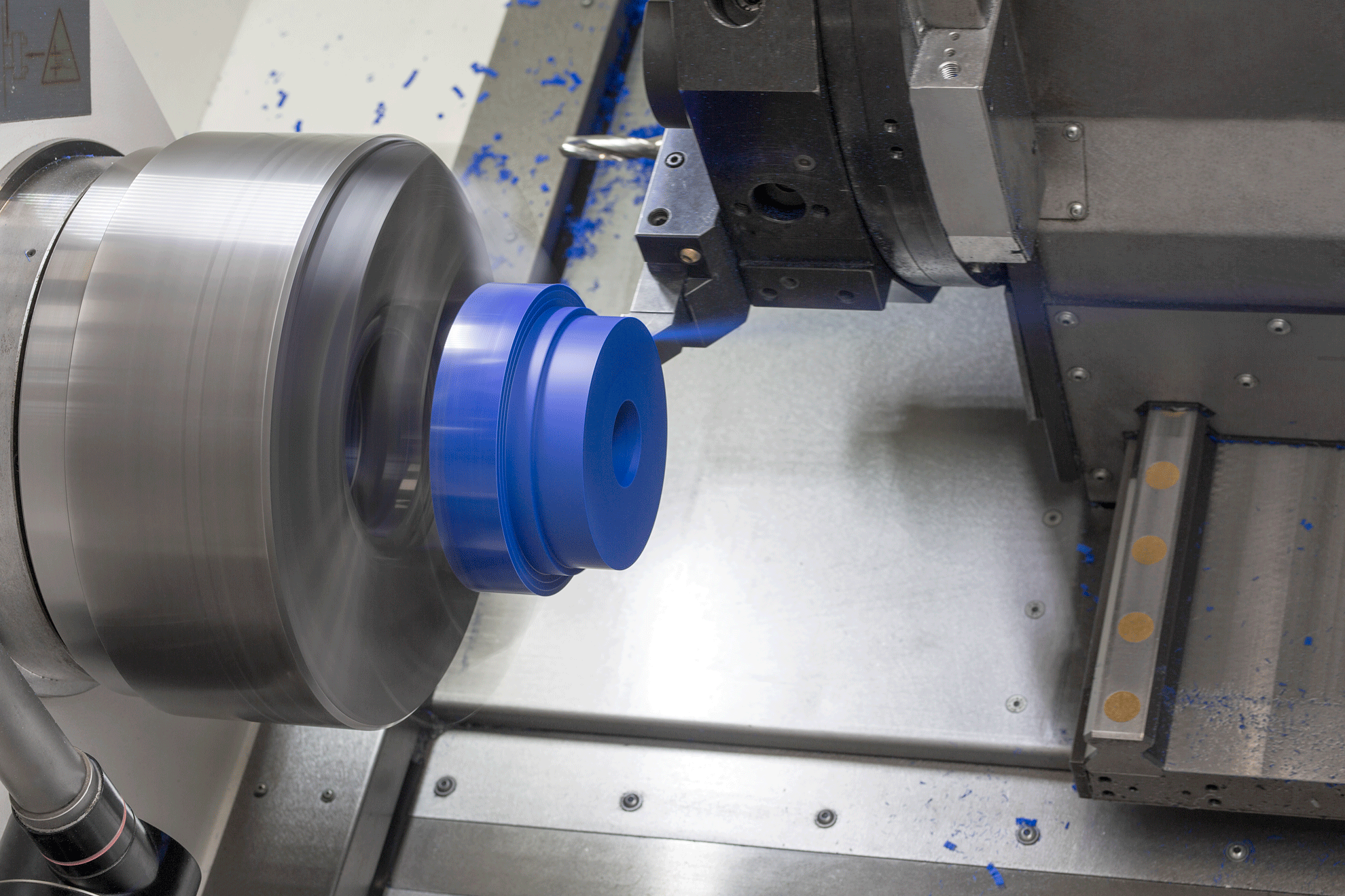 Blaues Kunststoffbauteil eingespannt in einer CNC-Drehmaschine.