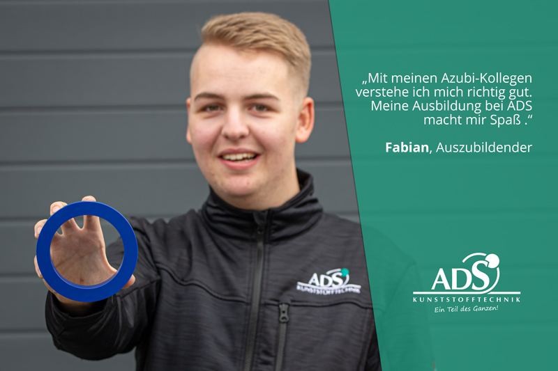 Fabian-Ausbildung-ADS-Kunststofftechnik Auszubildender bei ADS Kunststofftechnik hält lächelnd ein blaues Kunststoffbauteil in die Kamera.